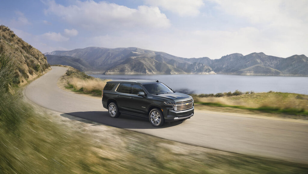 Chevrolet Tahoe driving on a mountain road beside a lake
